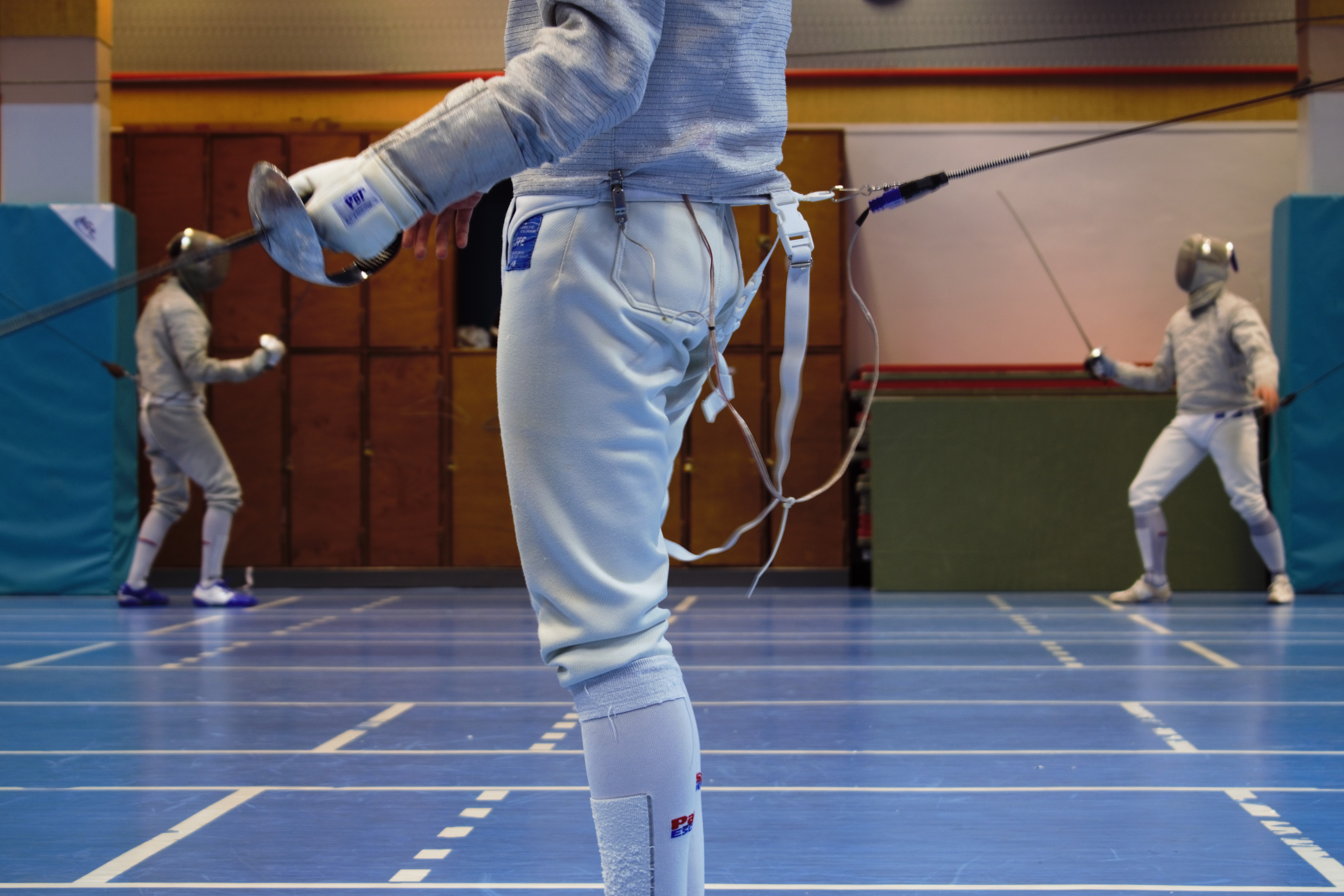 Fencing hall with a fencer's legs in the foreground.