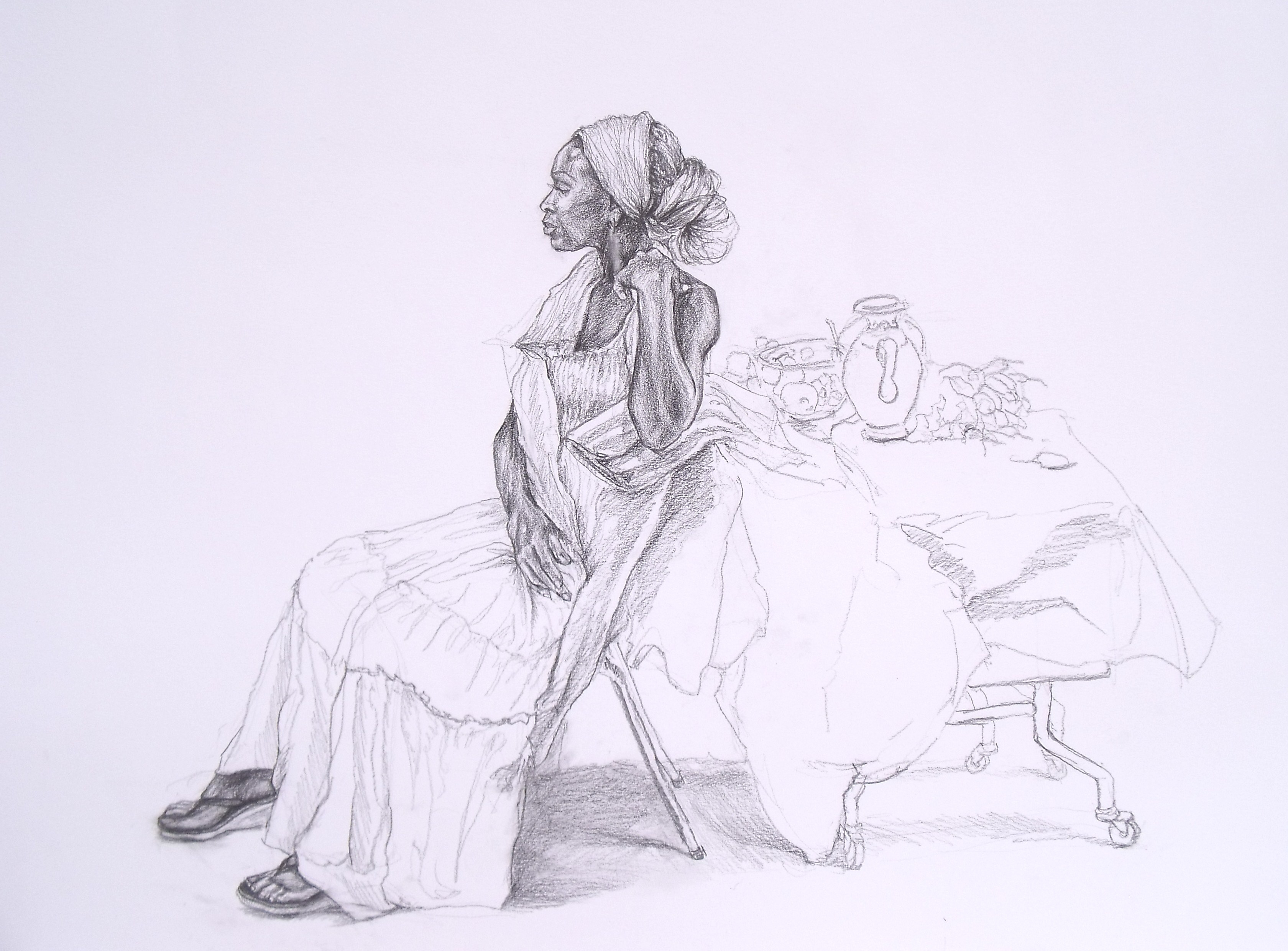 Une femme noire en robe longue assise de profile sur la chaise en tournant le dos à la table.