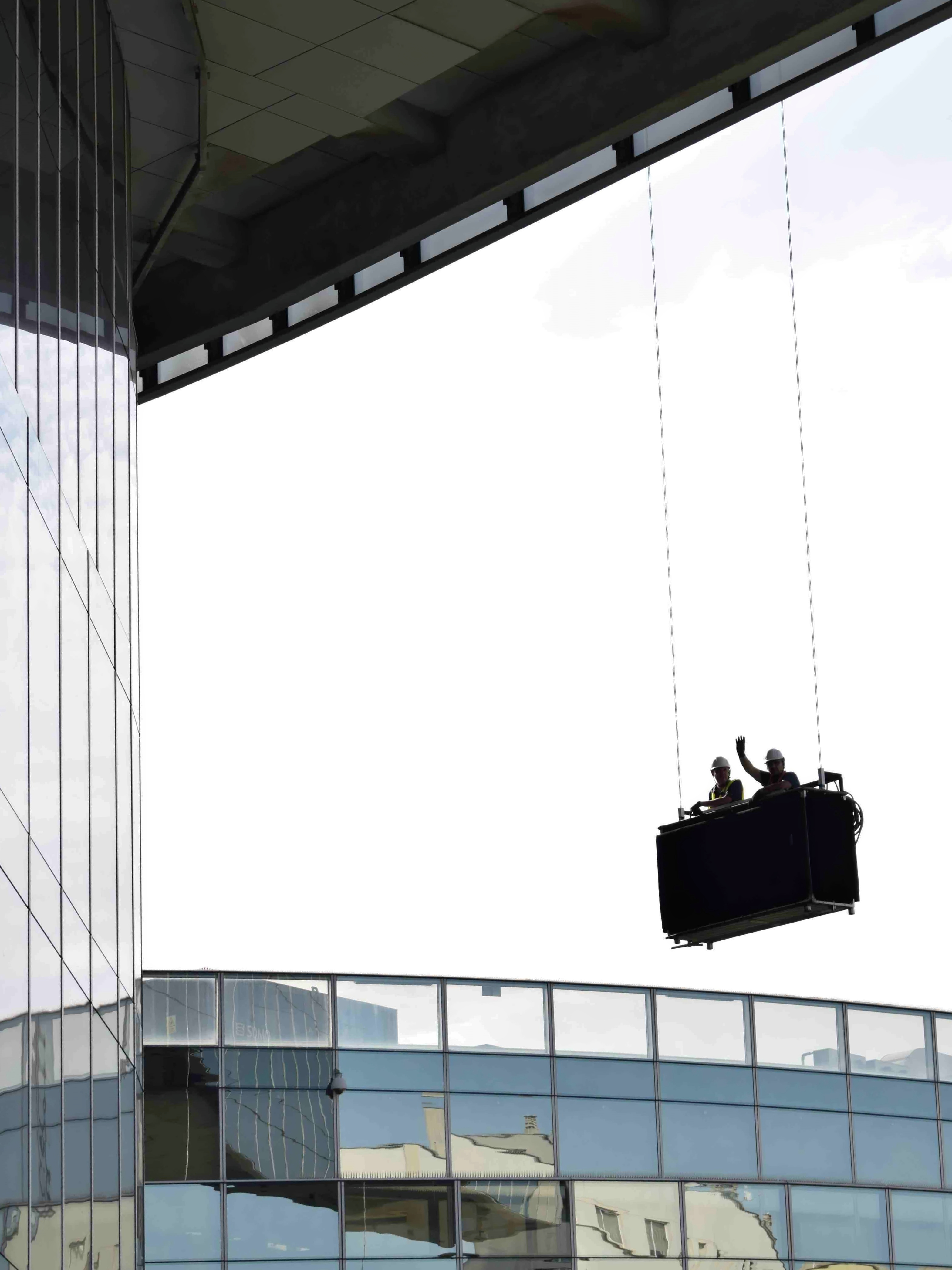Two workers on a construction platform suspended from the edge of a skyscraper