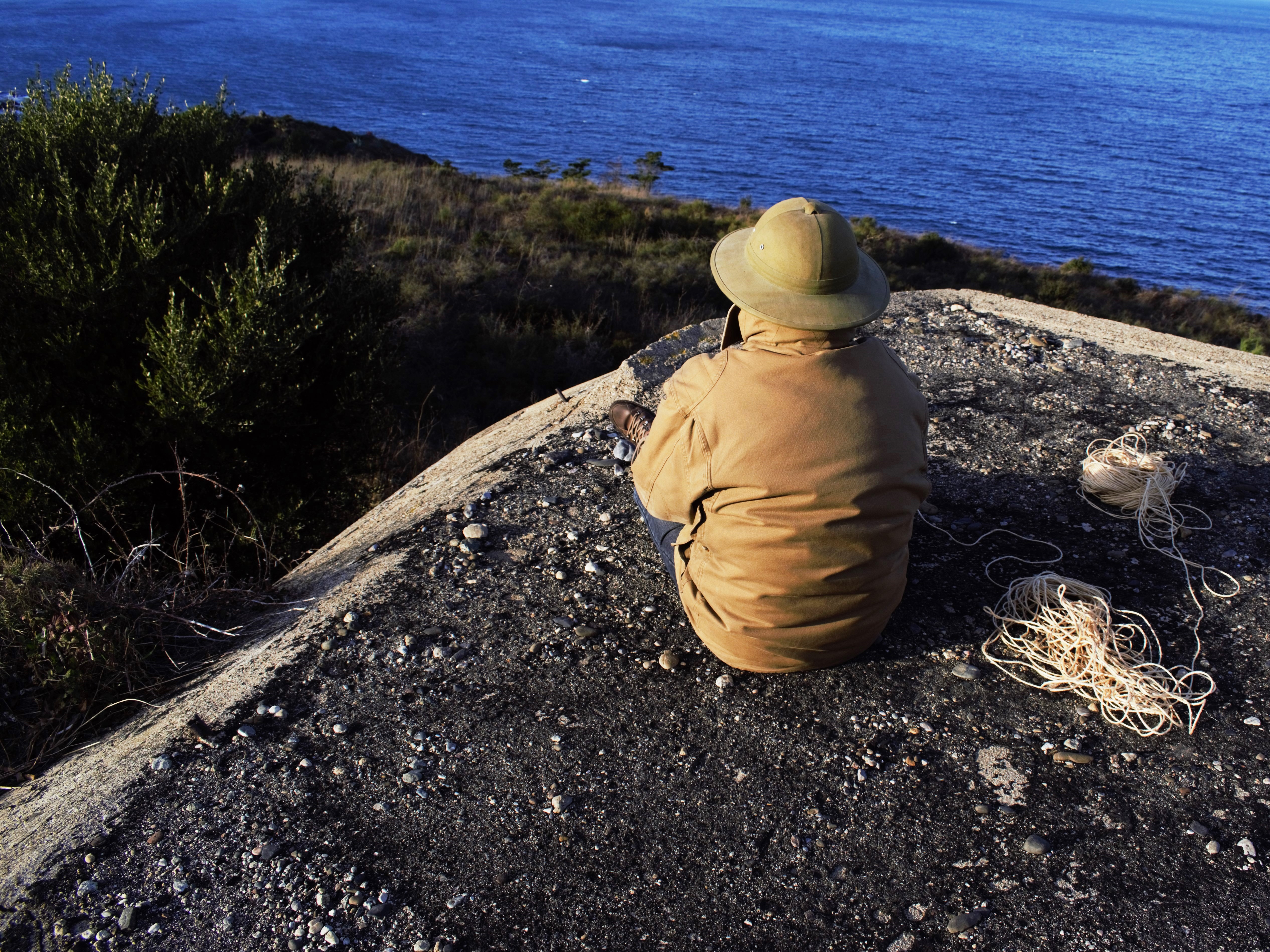 A person sitting with his back to the camera on a bunker overlooking the ocean