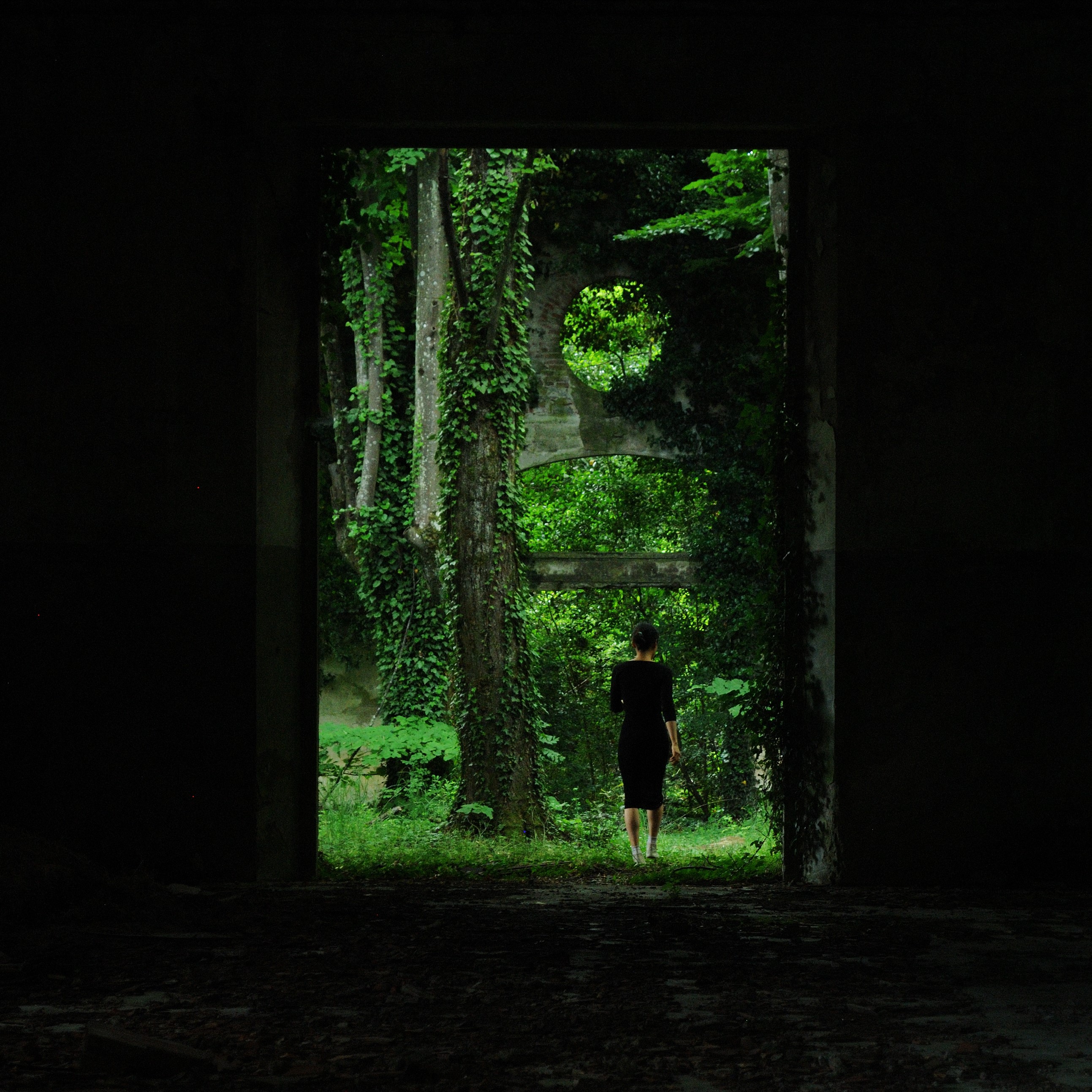 The interior in the dark with a woman standing at the threshold of the opening onto the forest