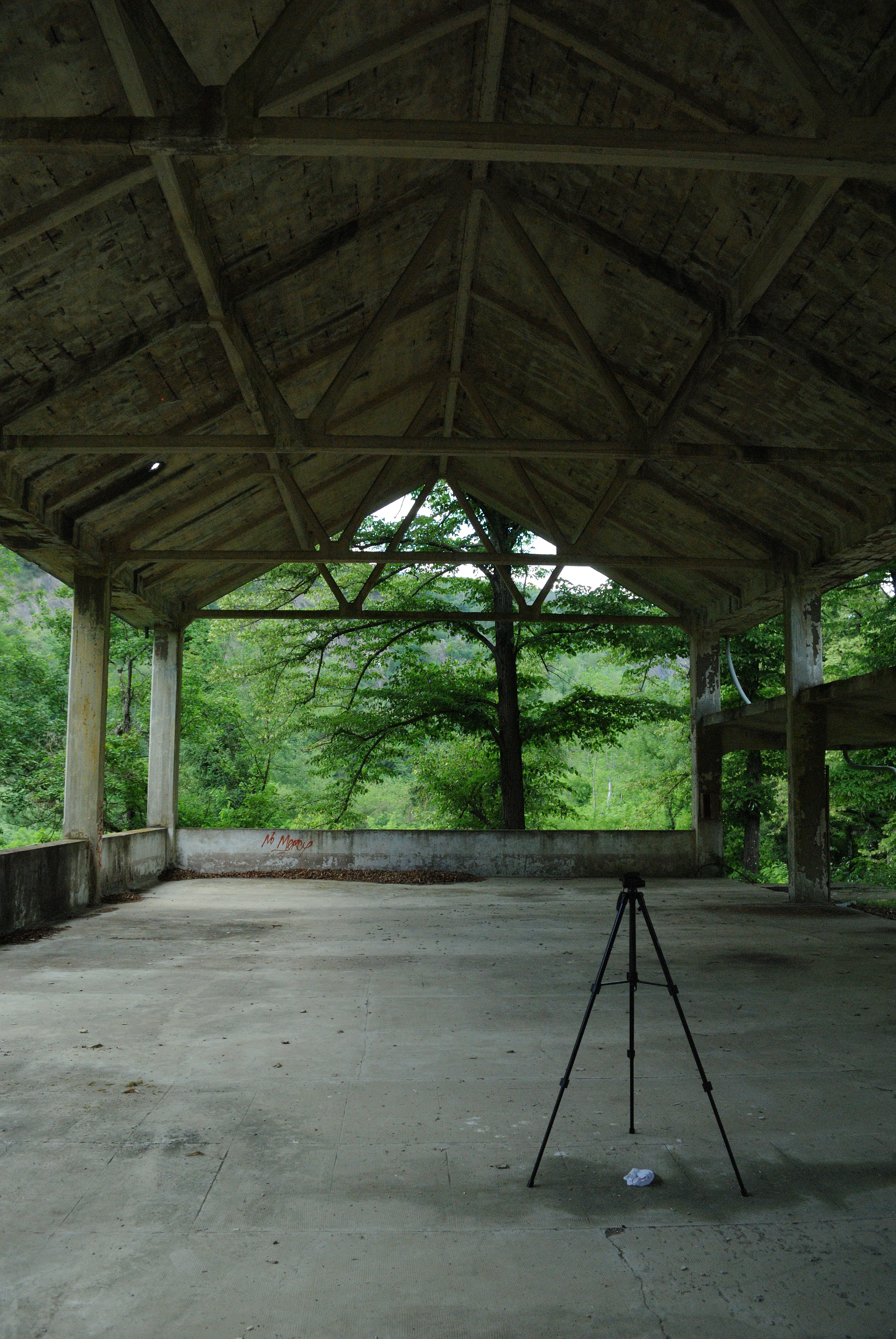 A large concrete hangar on the upper floor, open to nature, with a tripod placed in the foreground.