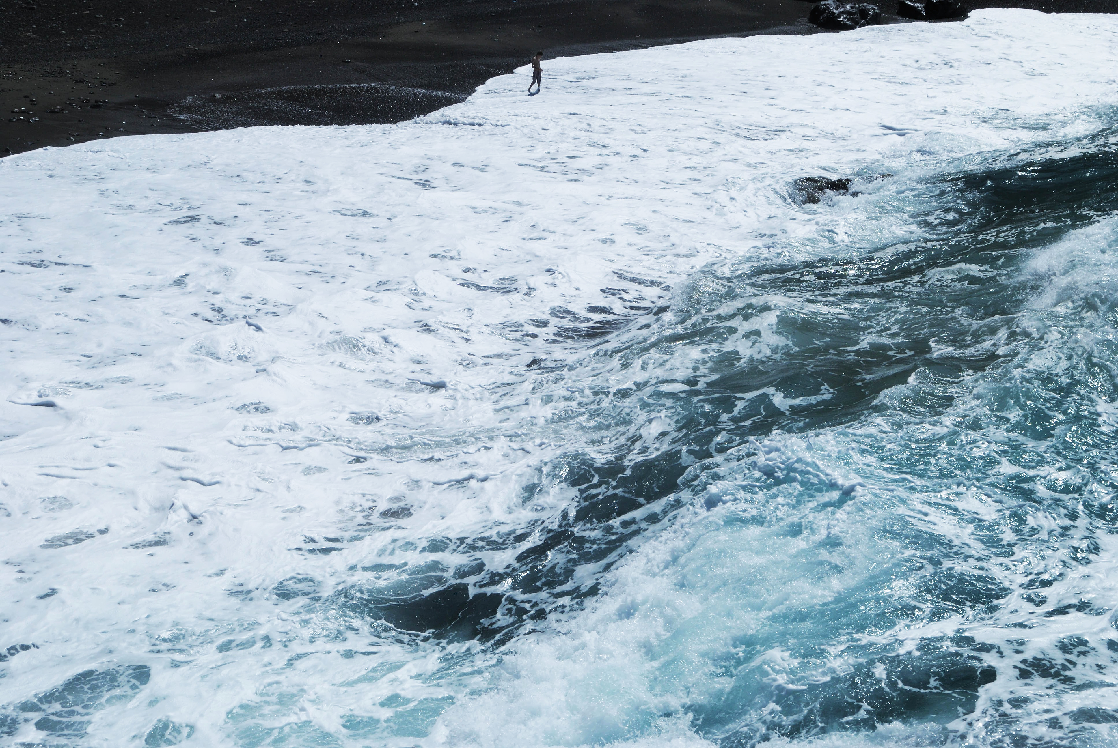 The black sand beach covered with waves breaking into white foam