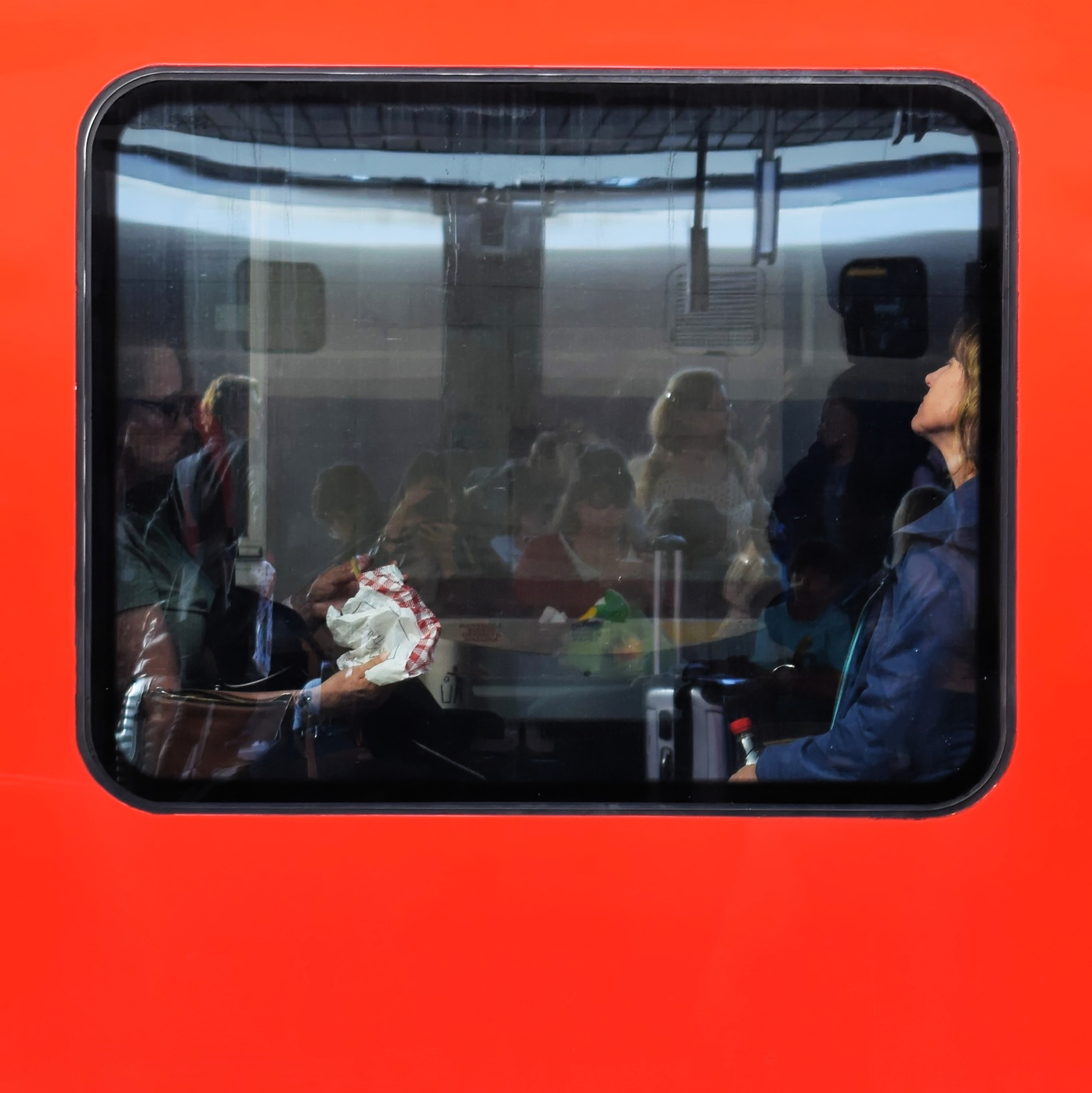A window of a red train showing the passengers inside and the reflection outside
