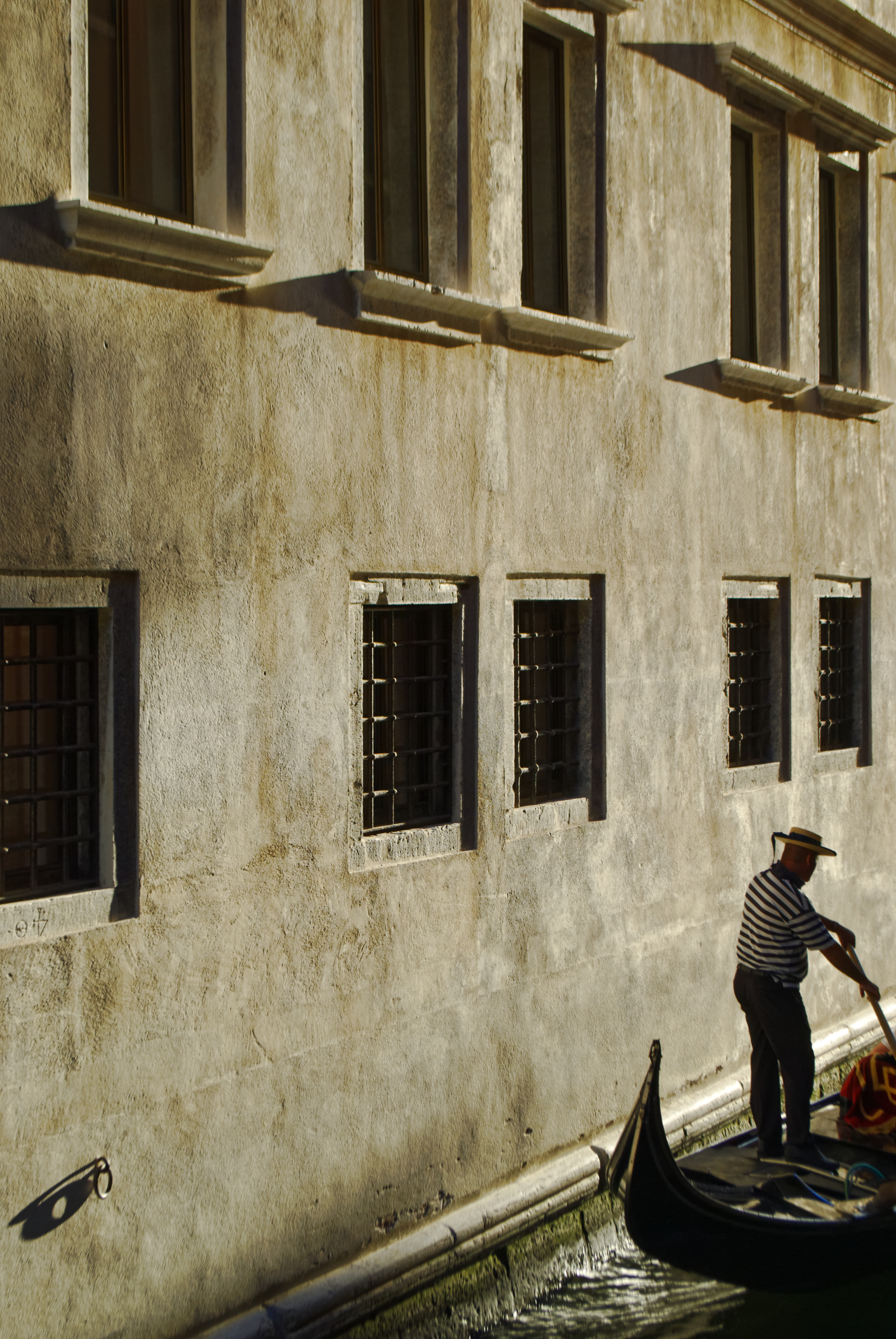 A gondolier rows his gondola standing up alongside a Venetian building bathed in golden light