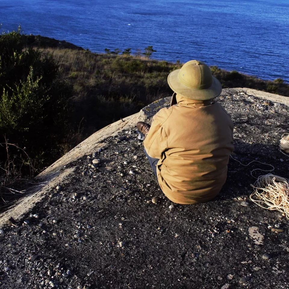 A man sitting with his back to the camera on a bunker overlooking the ocean